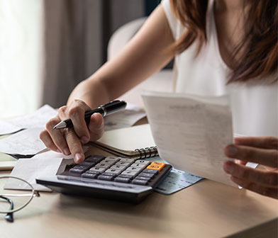 Une femme qui fait ses factures avec une calculette noire et ses lunettes sur la table