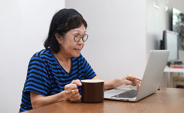 Une mamie qui regarde son ordinateur, une tasse à la main