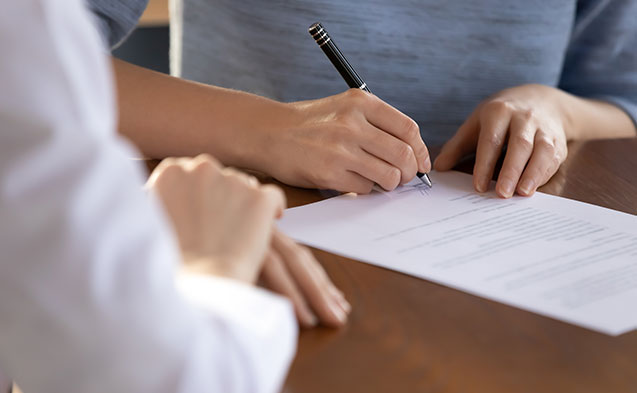 Une personne signant un document et son conseiller qui patiente à côté